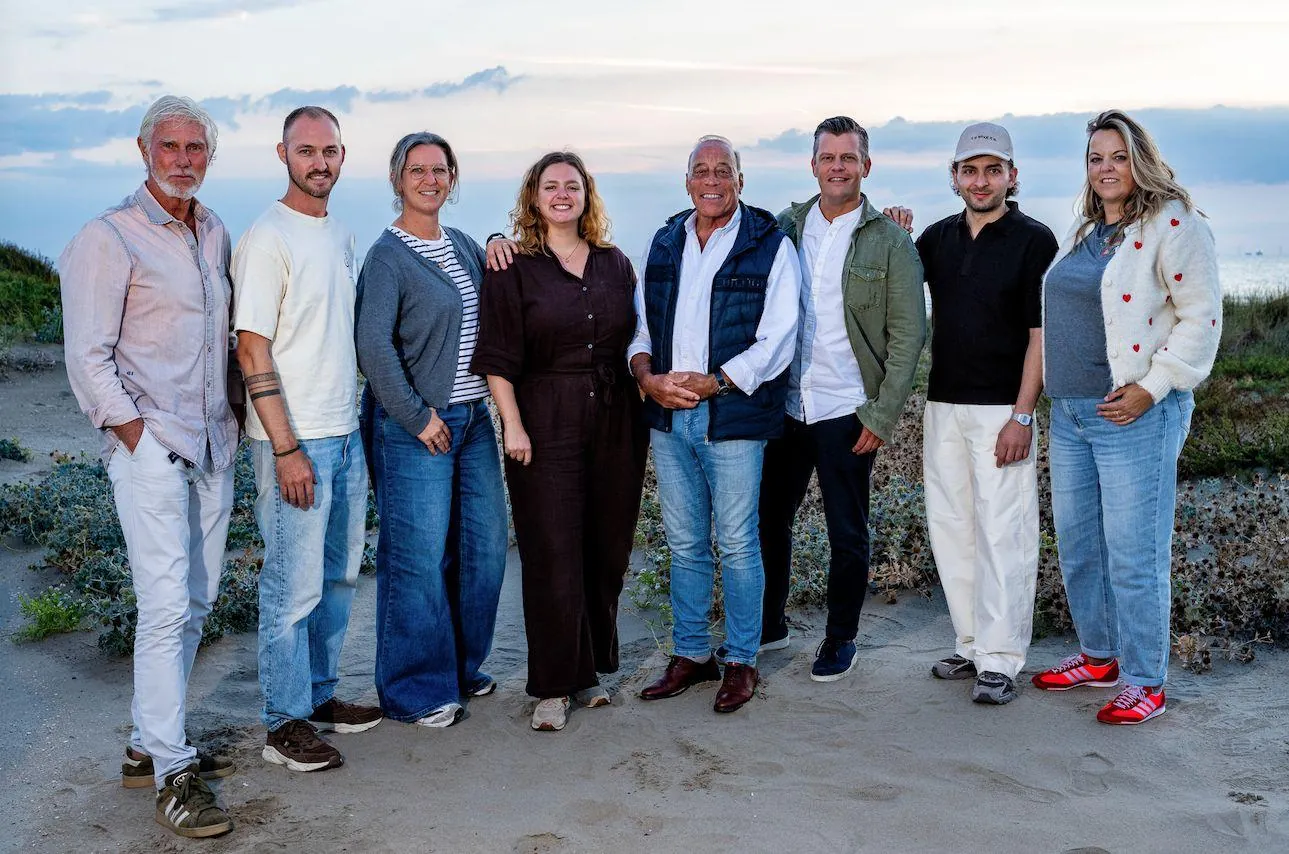 The Nieuwjaarsgala Noordwijk organisation: eight members standing side by side in the dunes by the sea, in evening light.